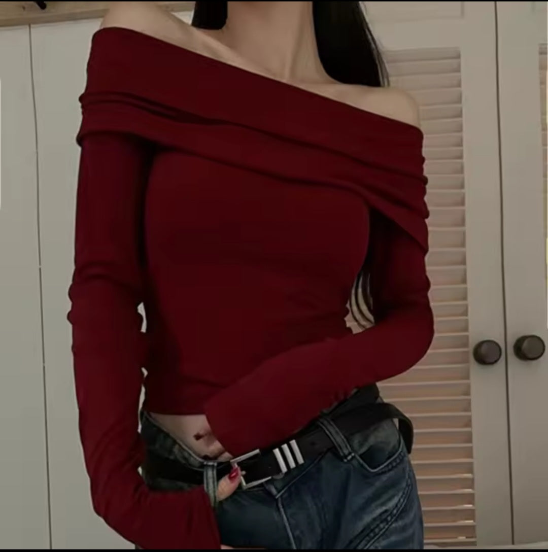 Person wearing a red off-shoulder top and blue jeans against a white wall.