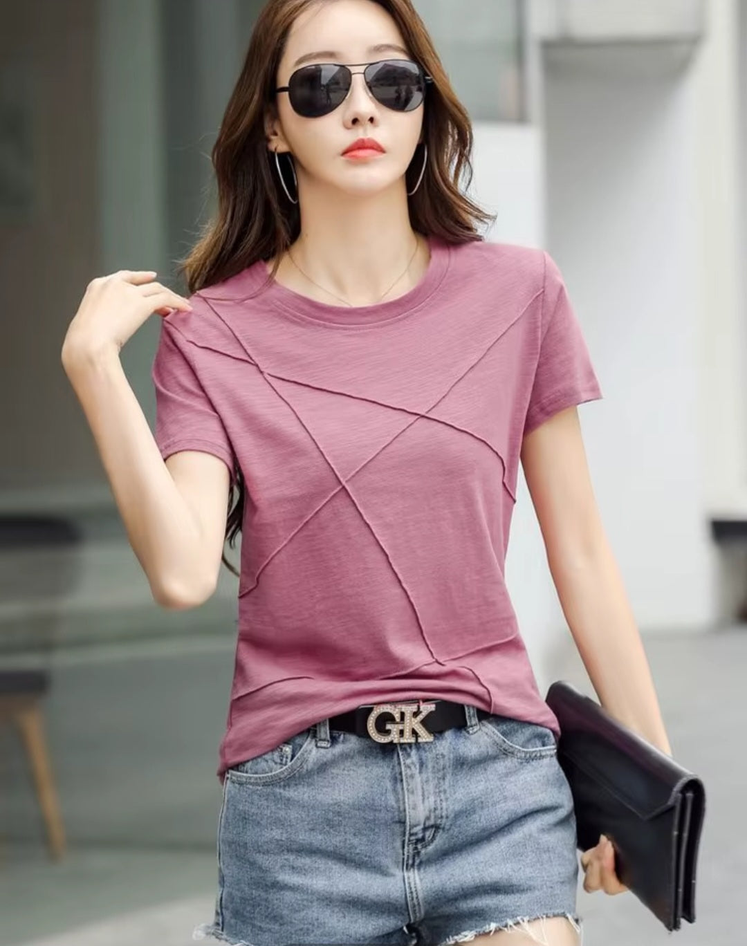 Woman wearing a mauve t-shirt and denim shorts with a blurred indoor background