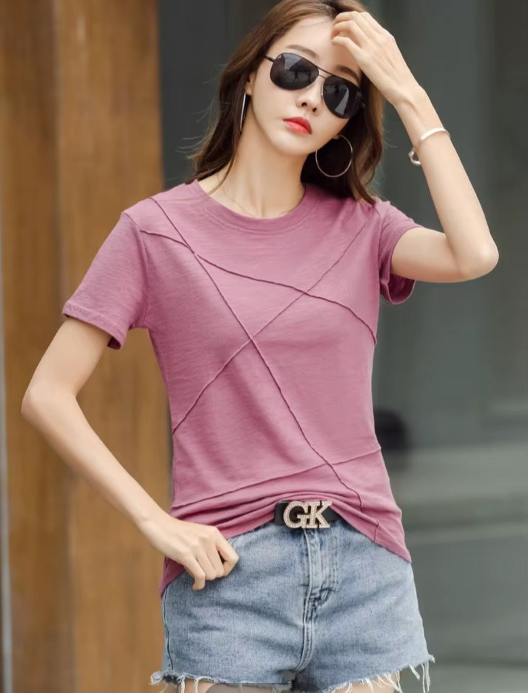 Woman wearing a pink t-shirt and denim shorts with sunglasses, standing against a blurred background.