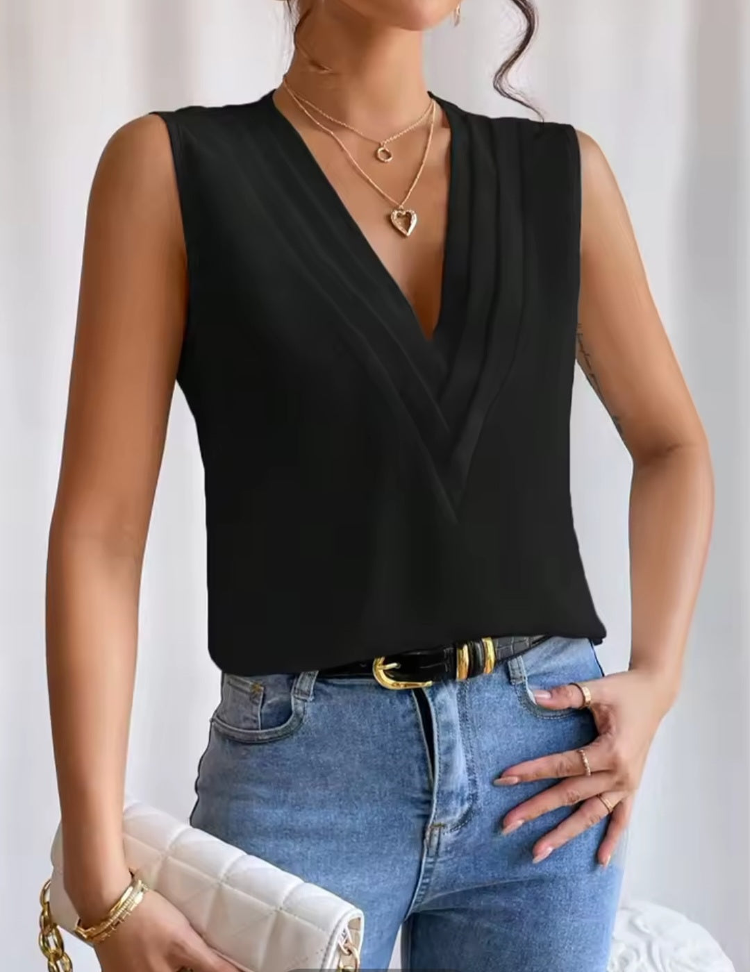 Woman wearing a black sleeveless top and blue jeans with a white background