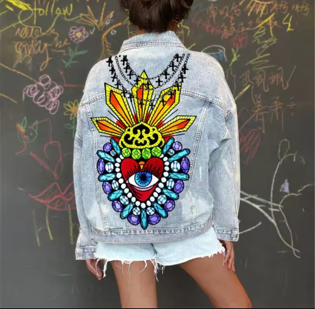 Person wearing a denim jacket with a colorful back design in front of a chalkboard.