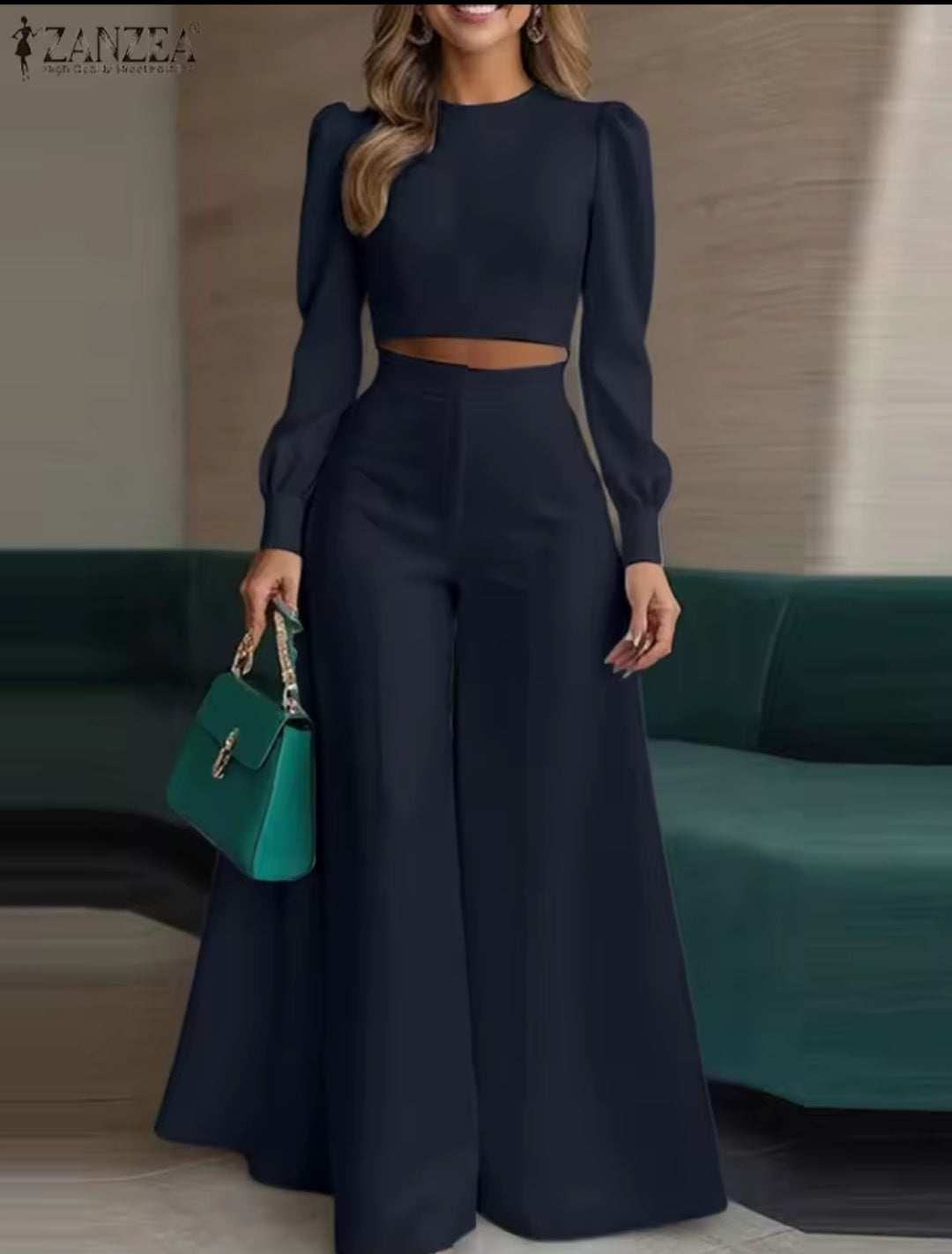 Woman in a navy blue outfit holding a green handbag in an indoor setting.