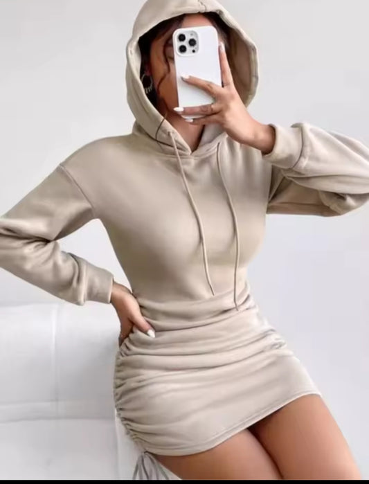 Person wearing a beige hooded dress holding a phone on a plain background