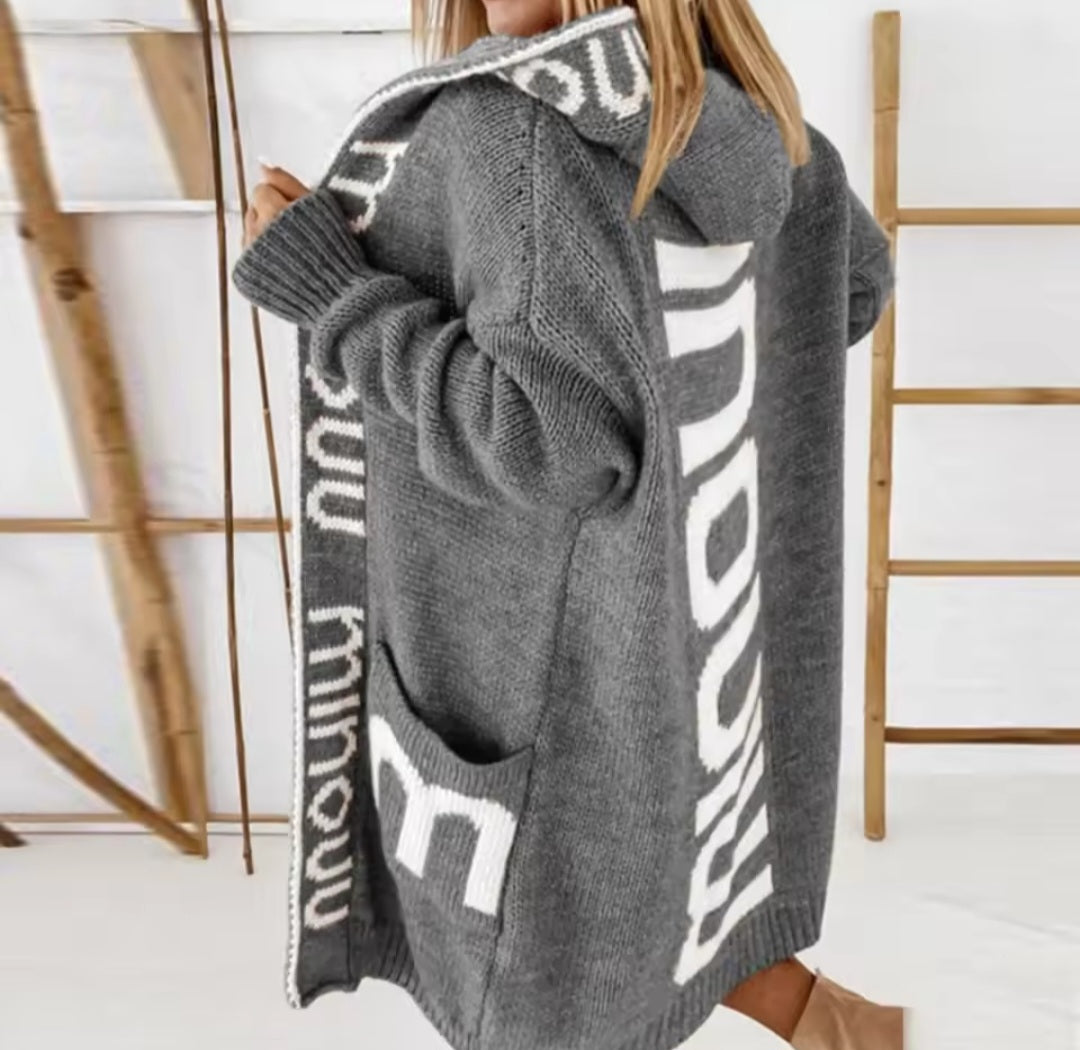 Gray cardigan with white text pattern worn by a person, against a minimal background.