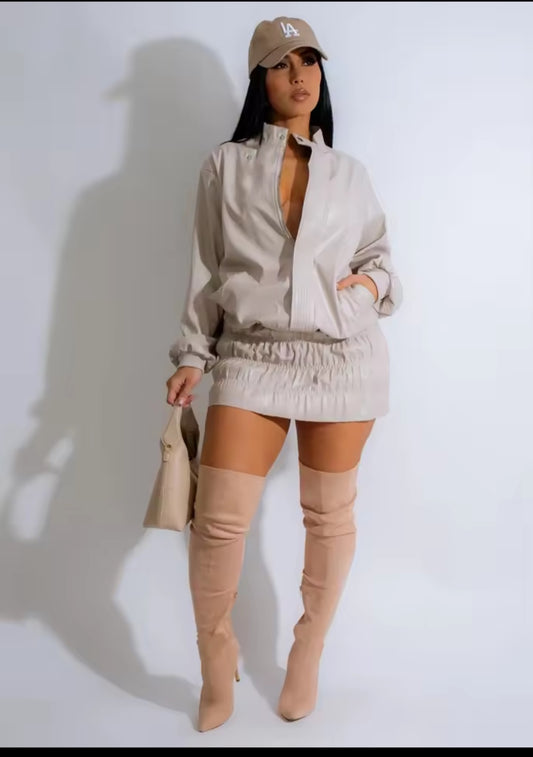 Woman wearing a beige outfit with a jacket, skirt, and knee-high boots on a white background