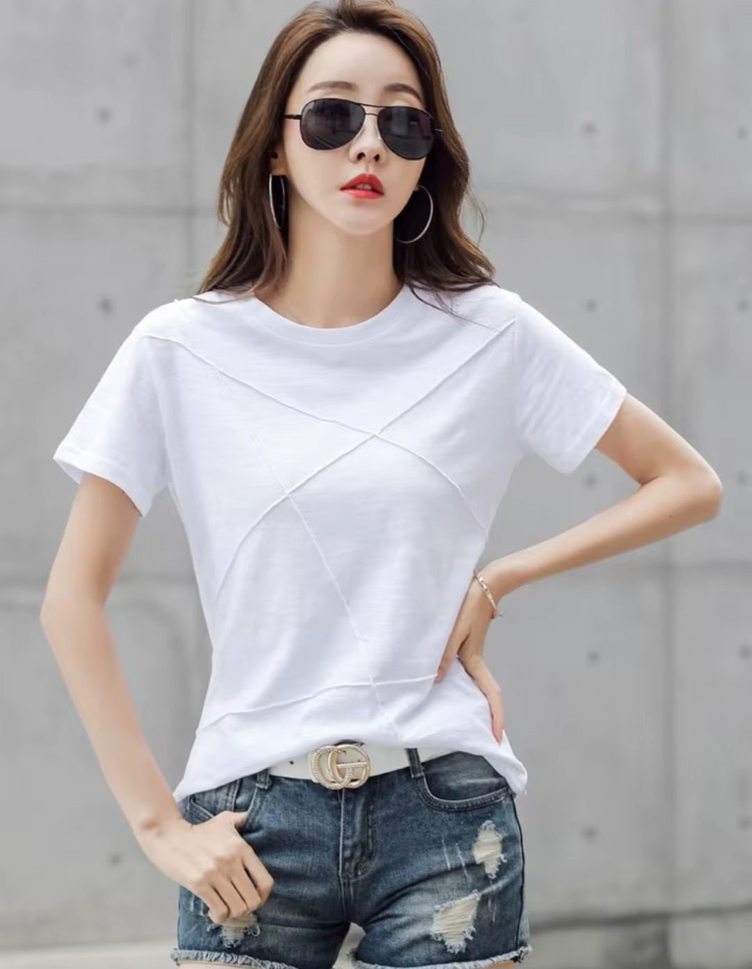 Woman wearing a white t-shirt and denim shorts with sunglasses against a gray background