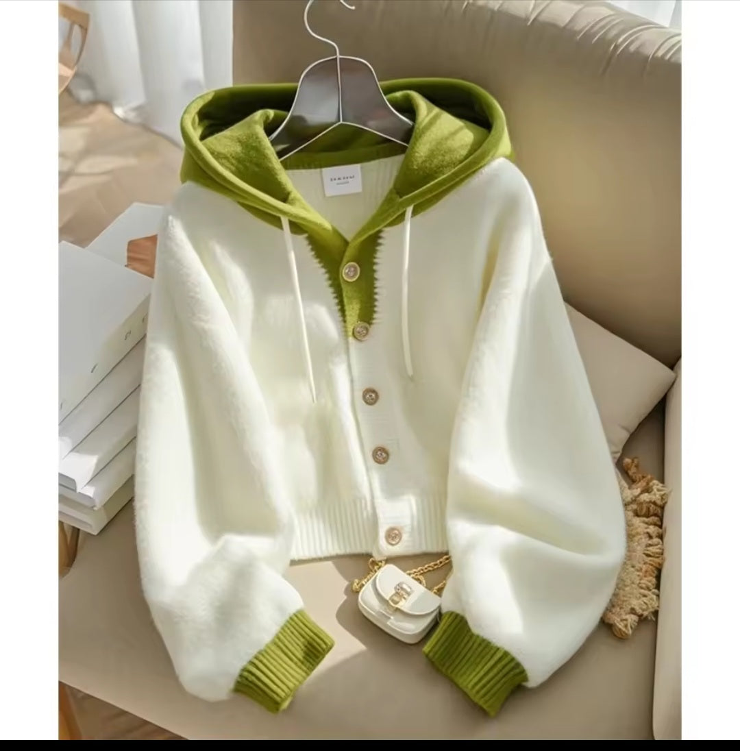 White cardigan with green trim on a hanger against a neutral background