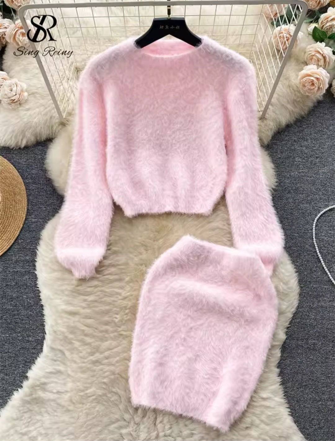 Pink fluffy sweater and skirt set on a textured surface with flowers in the background