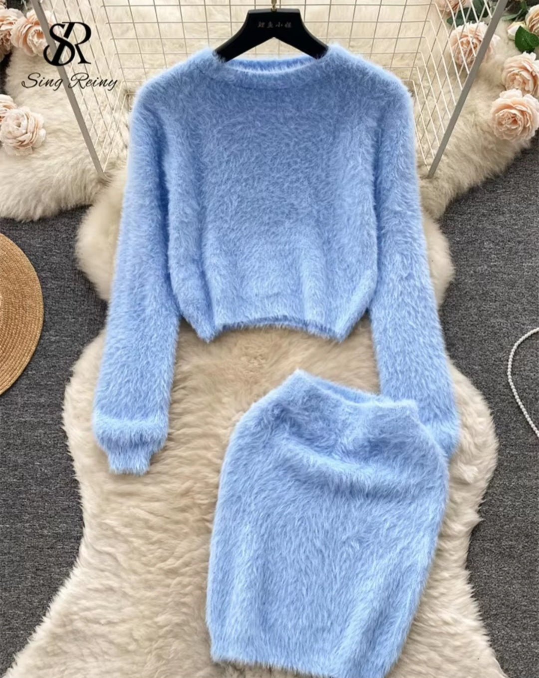 Light blue fuzzy sweater and skirt set on a textured surface with floral decorations.