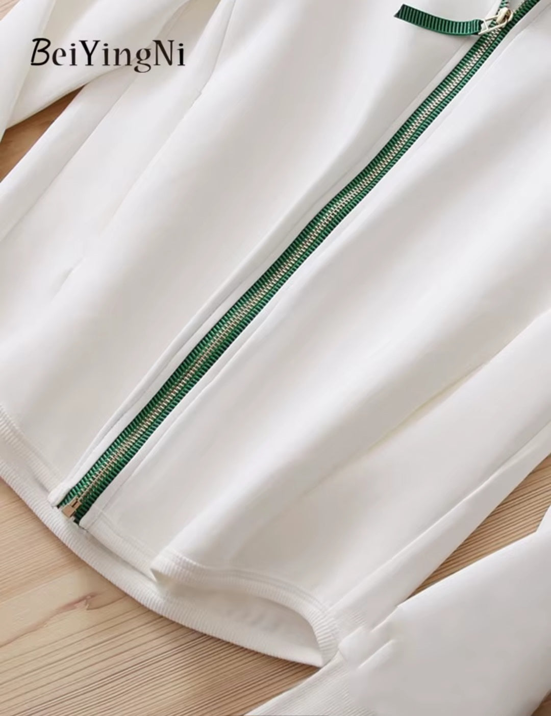 White pants with a green zipper on a wooden surface, featuring the brand 'BeiYingNi'.