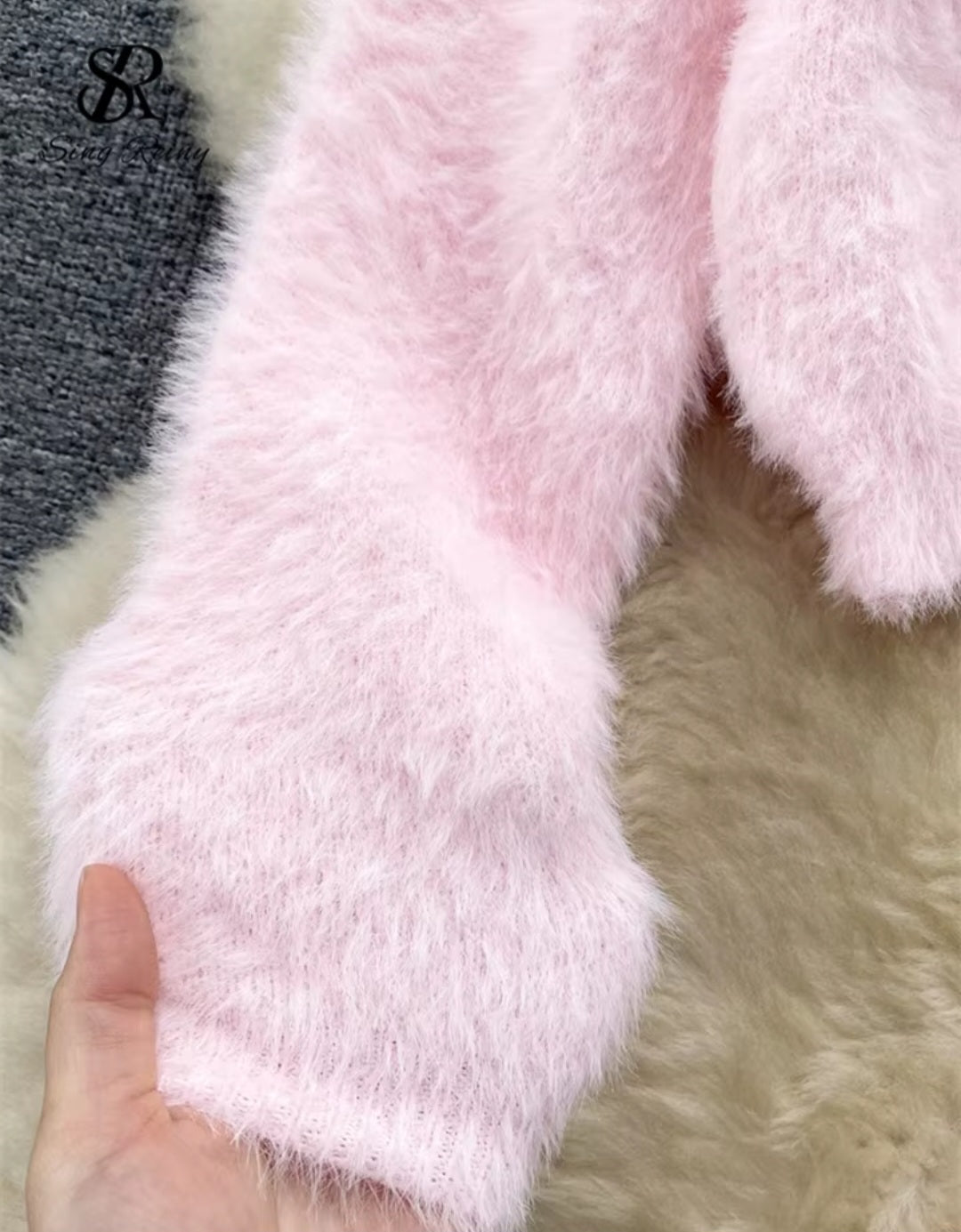 Close-up of pink fluffy fabric with a hand holding it, on a neutral background.