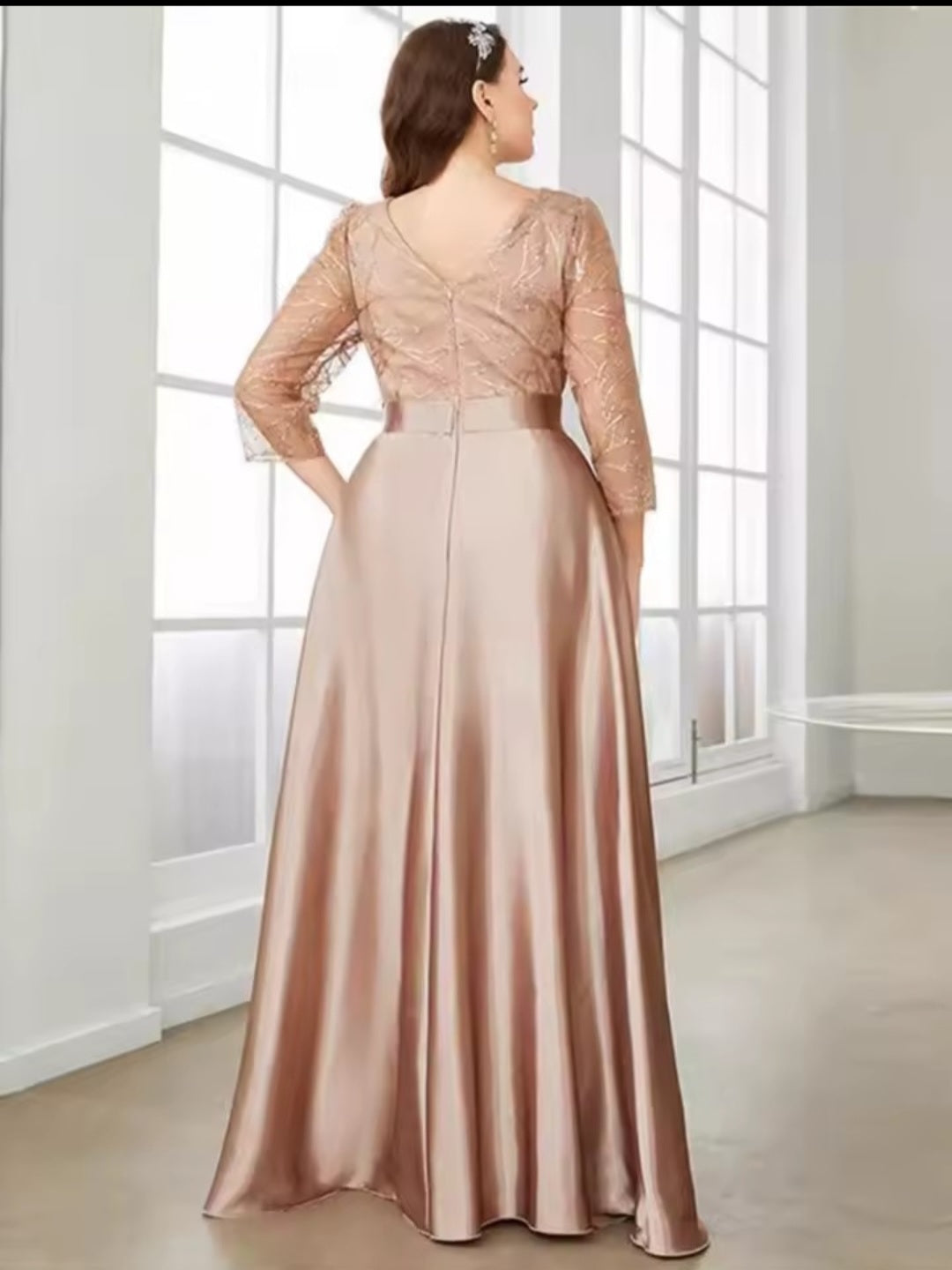 Woman wearing a long, elegant dress with lace top and satin skirt in a bright room.